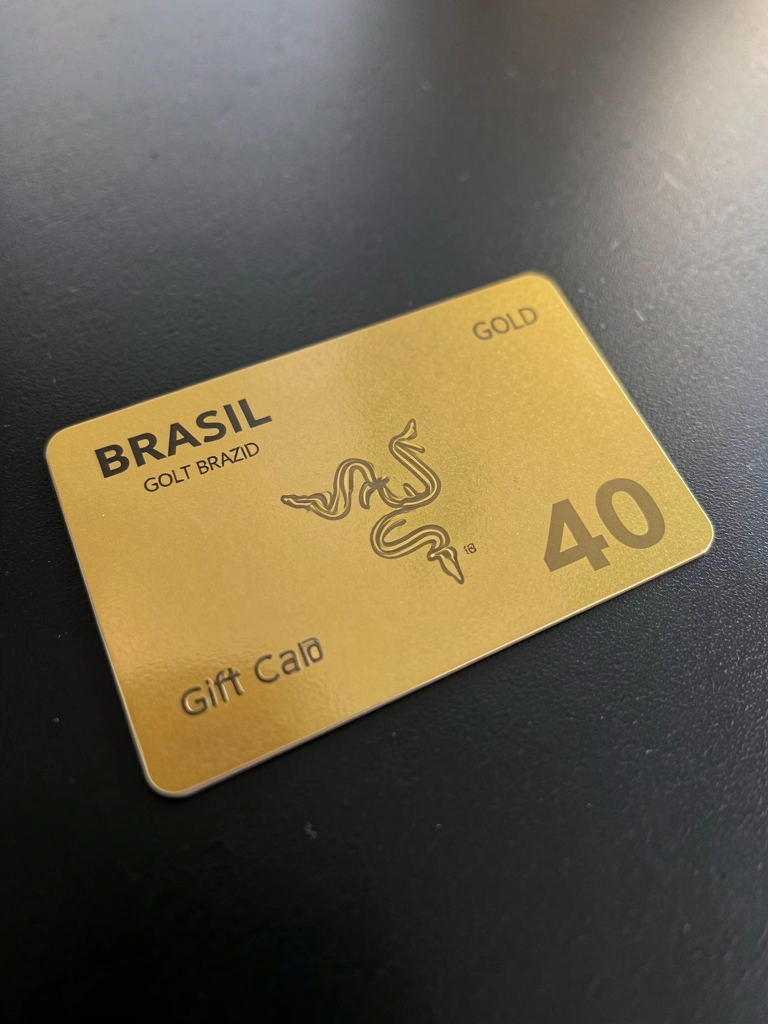 Cartão-presente Razer Gold Brasil metálico com detalhes reflexivos sobre superfície preta, iluminado por luz natural suave.