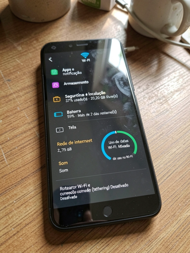 Smartphone sobre mesa com ícone de roteador Wi-Fi na tela, ao lado de notebook e xícara de café.