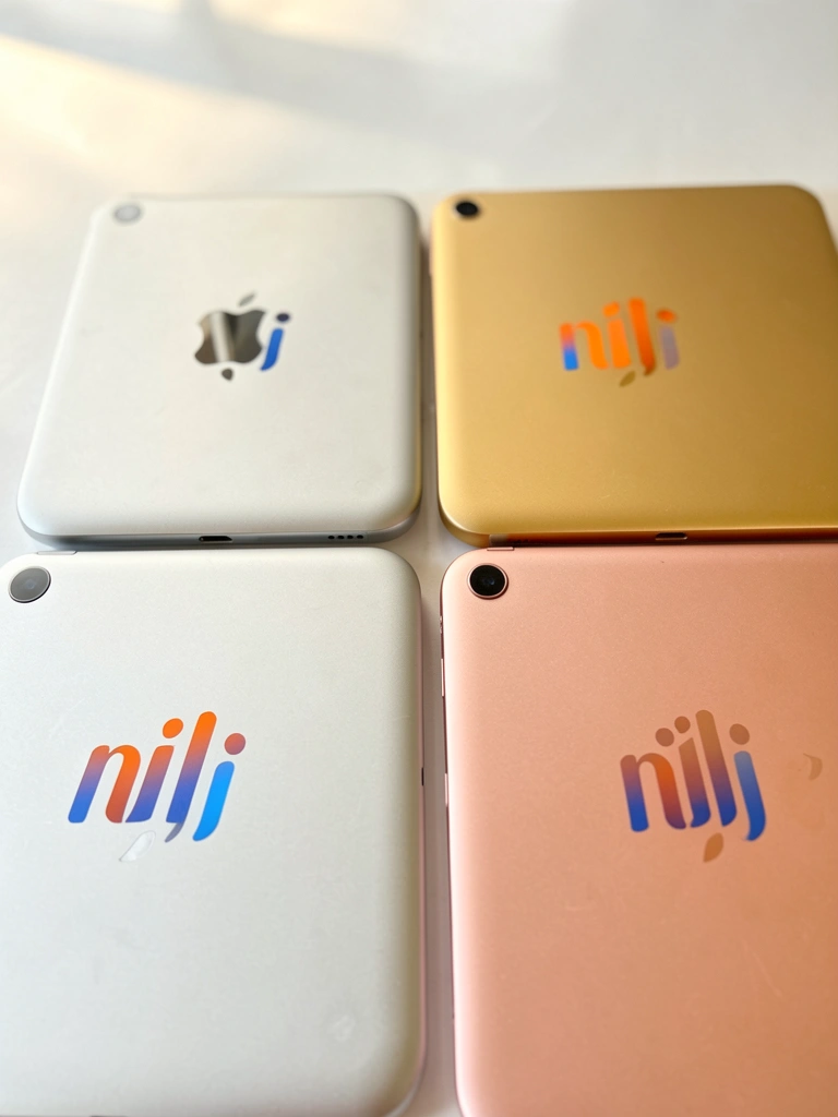 Quatro iPads mini prata, dourado, cinza claro e rosé dispostos em quadrado sobre fundo branco, com logotipo laranja e azul, refletindo luz natural.