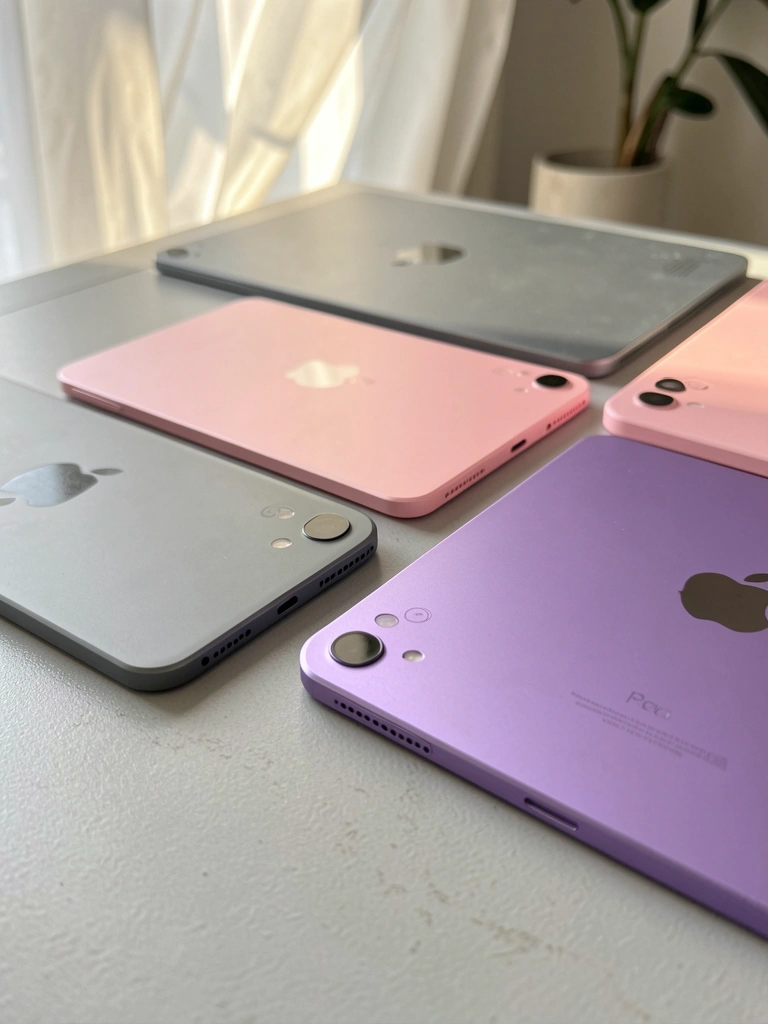Quatro iPad Minis nas cores Slate Gray, Pink, Purple e Starlight sobre superfície cinza clara, com luz natural e fundo arejado.
