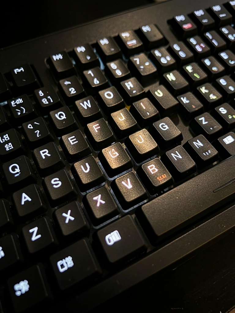Teclado mecânico preto com teclas iluminadas, refletores metálicos e fundo escuro, close-up detalhado.