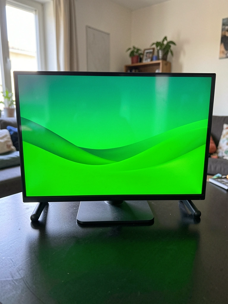 Monitor de 32 polegadas sobre rack de madeira, ao lado de controle remoto e soundbar preta.